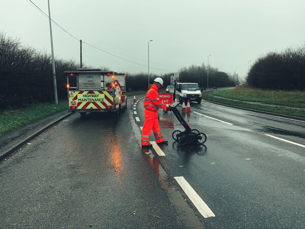 A workman manoeuvring a tool across a road